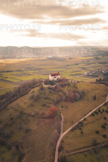 A red church roof on a hill with a view of vast fields under a cloud cover, Wurmlinger Chapel,