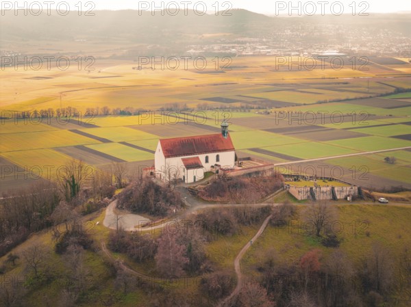 A church with a red roof towers over a vast mosaic of fields in sunlight, Wurmlingen Chapel,