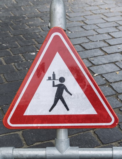 Triangular warning sign on cobblestones depicting a stylized figure with a tray, province of