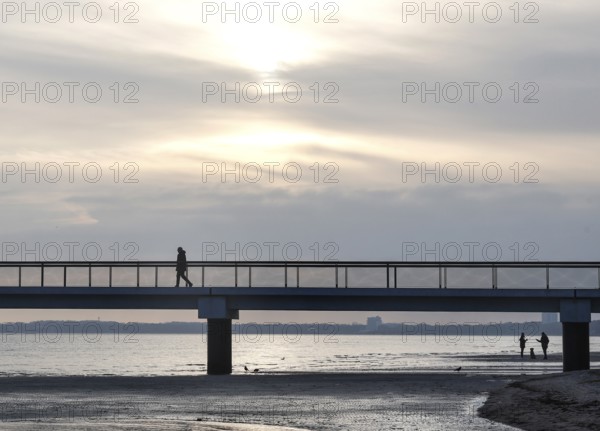 Silhouettes of people on and under a pier, low tide, wave and ripple patterns in wet sand, sunrise,
