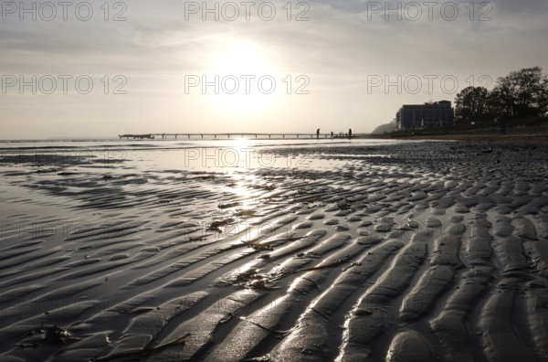 Low tide, wave and ripple patterns in wet sand, long pier in the background, sunrise, Scharbeutz,