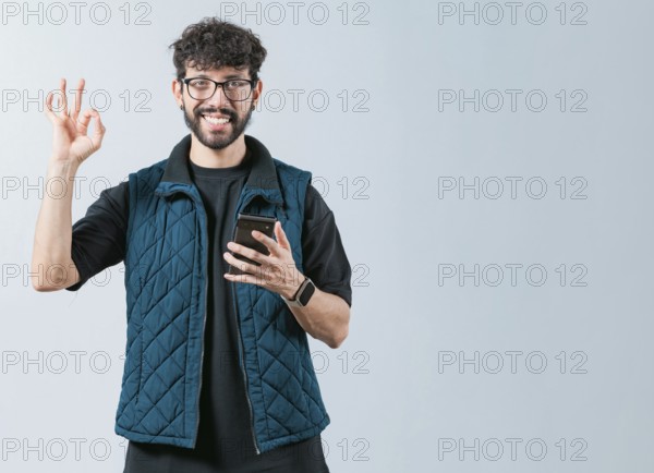 Attractive man in glasses holding phone gesturing OK. Smiling handsome man holding phone and