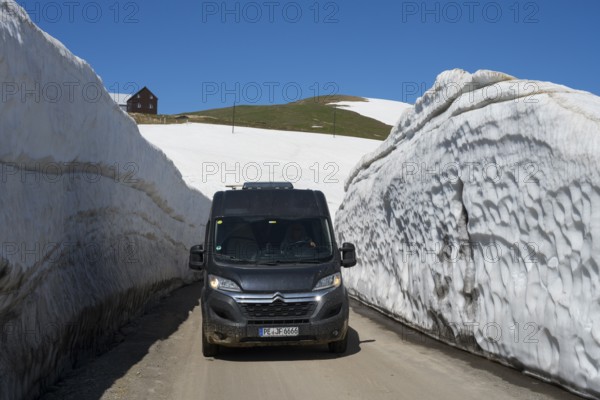 A van drives through thick snow walls on a mountain road under a blue sky, motorhome, camper on a