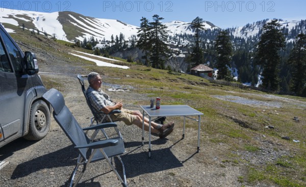 A man relaxing next to a van in a sunny mountain landscape, view from Goderdzi Pass, Ajara region,