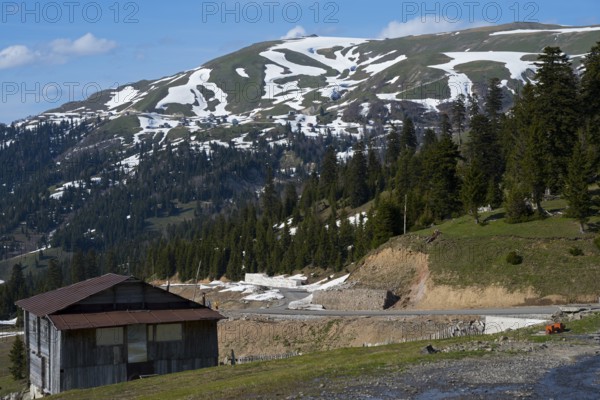 A mountainous landscape with snow-covered hills, forest and a hut in peaceful nature, on the