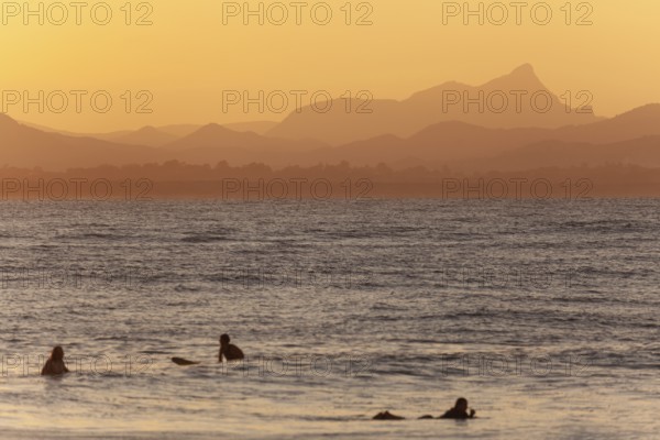 Red sunset on Wategos Beach with surfers in the ocean. Mt. Warning, Wollumbin in the background of