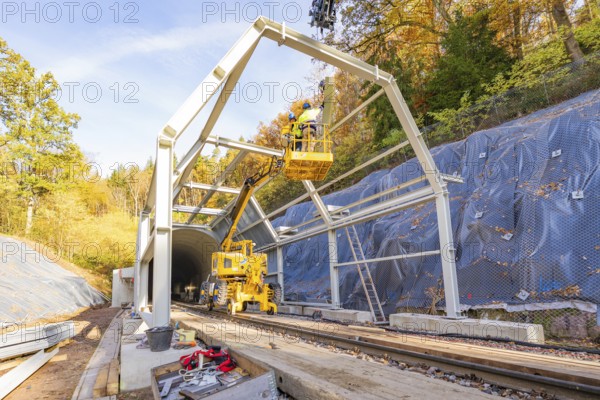 Construction work on a tunnel opening with cranes and workers against an autumn backdrop, Hermann