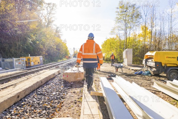Construction workers in glowing vests work on a railway construction site under clear skies,
