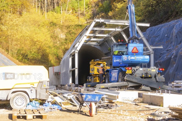 Construction site in front of a tunnel with machinery surrounded by autumn trees, Hermann Hesse