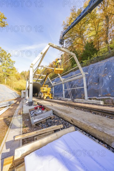 Crane lifts construction material for a tunnel surrounded by autumnal forest and blue skies,