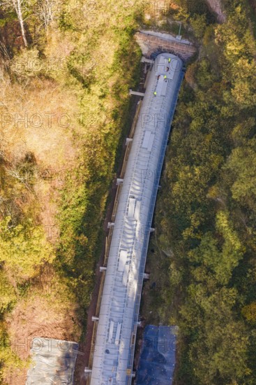 Tunnel construction viewed from above, nestled in a dense autumn forest with colorful leaves,