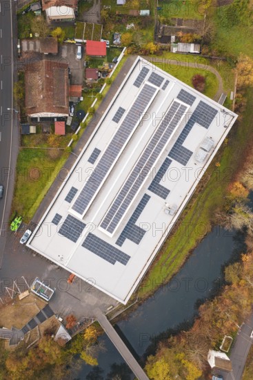 Building with solar roof, surrounded by a village and river, viewed from the air in an autumn