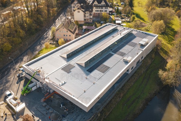 Modern building with solar panels, surrounded by a river and autumnal nature, viewed from the air,