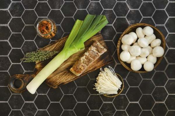 Fresh leeks, bacon and thyme on a wooden cutting board. A jar of pickled honey mushrooms and fresh