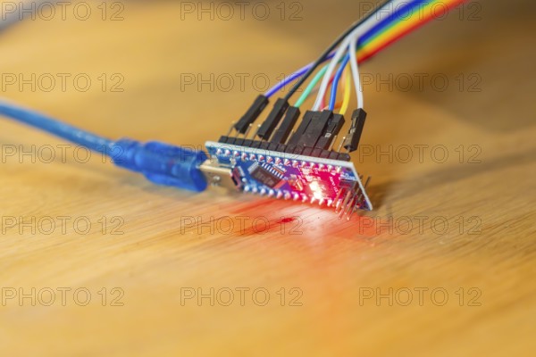 Small circuit board glows red, connected to USB cable, on wooden table, Jugend Forschungszentrum