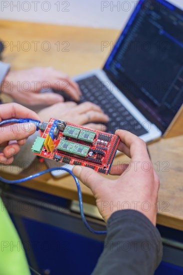 Person holding circuit board while someone is programming on a laptop, Jugend Forschungszentrum