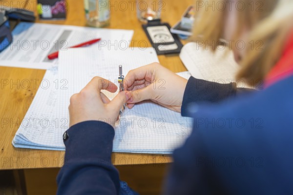 Person writing notes on checkered paper at a wooden table, Jugend Forschungszentrum Nagold, Calw