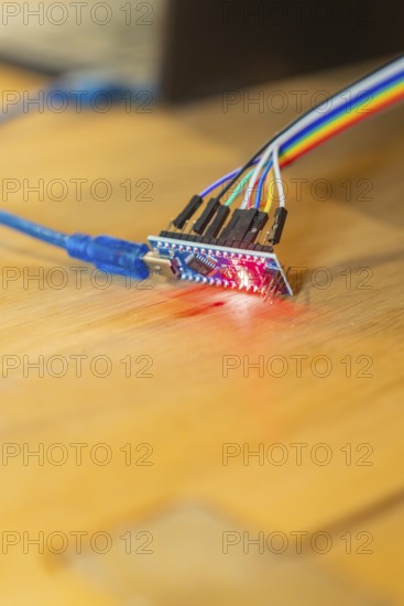 Red glowing circuit board connected to USB cable on wooden table, Jugend Forschungszentrum Nagold,