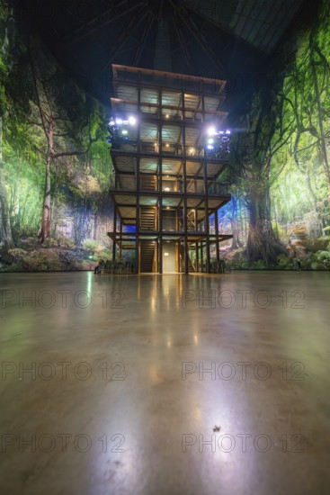 A wooden tower stands in front of a green illuminated artificial jungle backdrop, Amazonia