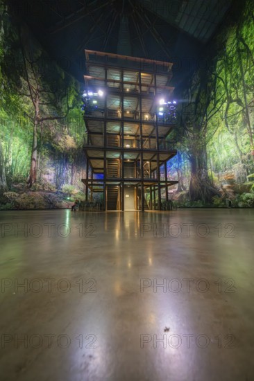 An artificial jungle installation with a green illuminated wooden tower in a hall, Amazonia