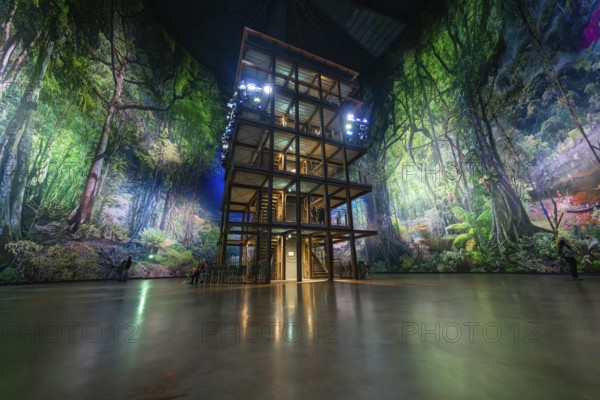 A multi-storey timber building in a glowing green artificial forest installation, Amazonia