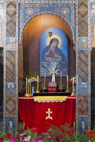 Religious altar with icon and candles richly decorated with flowers in a decorated wall niche,