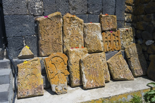 Historical, engraved stones with flowers on concrete in front of a wall, cross stones at Sevanavank
