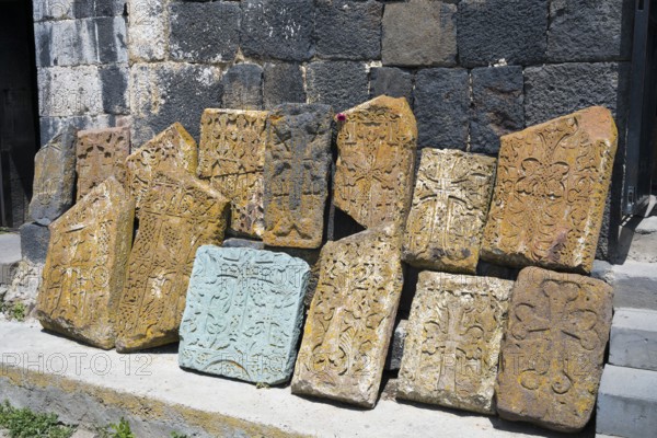 Decorated, engraved tombstones lean against an old wall, cross stones at Sevanavank Monastery,