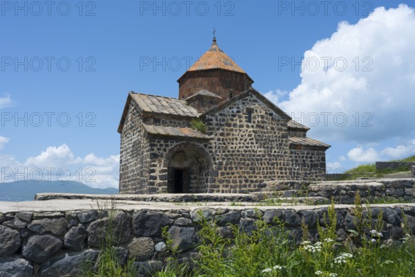 Historic stone church with orange roof against blue sky and white clouds, Sevanavank Monastery,