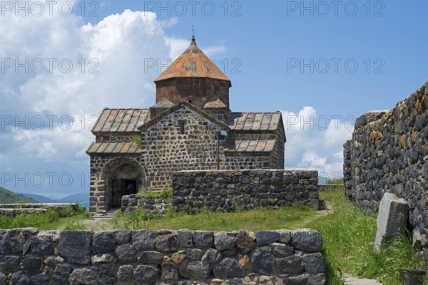 Front view of a historic stone church with brick wall and overgrown landscape, Sevanavank