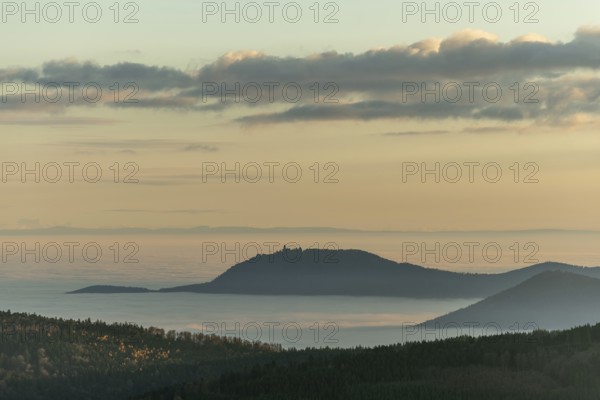 The landscape of hills and mountains is illuminated by a gentle sunset. Sea of fog in distance