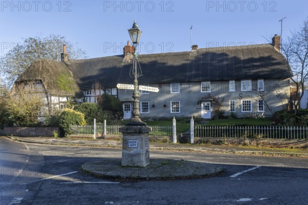 Historic signpost with direction arrows, thatched cottages in village of Pewsey, Wiltshire,