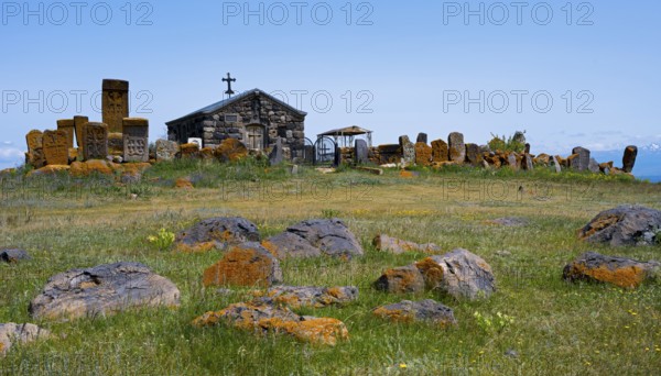 Small chapel surrounded by old tombstones on a hilly meadow under a blue sky, khachkar at the