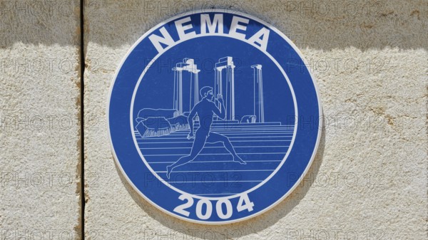 Blue sign with ancient columns and a runner in front of a stone wall, Ancient Stadium, Nemea,