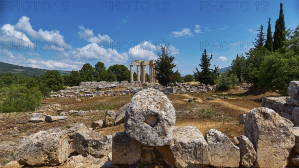 Ancient temple columns in an open field with surrounding trees and mountains in the background,