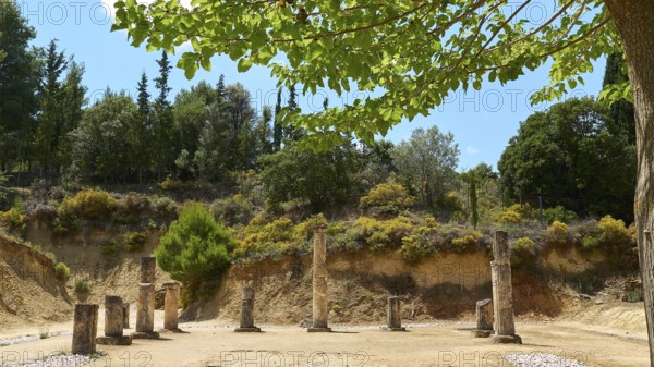 Ancient ruins with multiple pillars nestled in a lush green landscape under cloudy sky, Ancient
