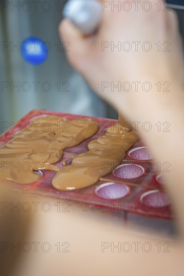 Close-up of a hand pouring liquid chocolate into a mold, Christmas baking, Haselstaller Hof,