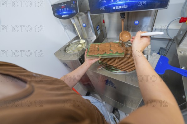 Person pouring liquid chocolate into a green mold next to a chocolate tempering machine, Christmas