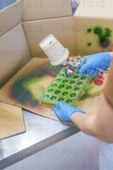 Person spraying green paint into a recessed mold on a cardboard table, Christmas baking,