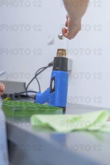 Person uses a blue heat gun to process green objects on a workbench, Weihnachtsbacken, Haselstaller