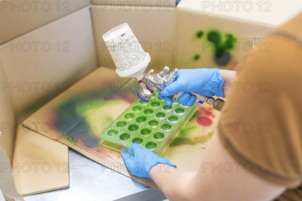 Person spraying green paint into a mold on a craft table surrounded by cardboard, Christmas baking,