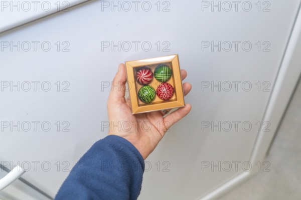 Person holding a chocolate box with patterned chocolates on a light background, Christmas baking,