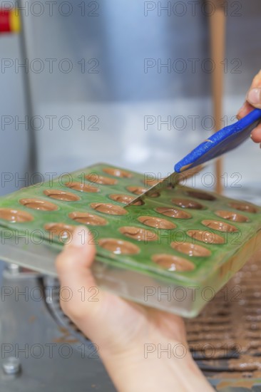 Hand spread chocolate evenly in a green mold with a blue spatula, Christmas baking, Haselstaller