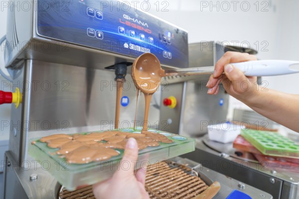 Chocolate filling is poured into molds from a tempering machine, Christmas baking, Haselstaller
