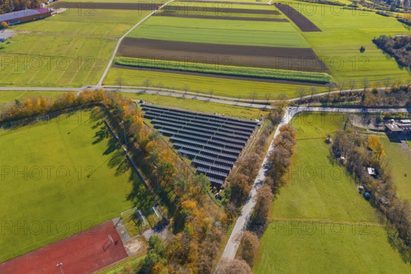 Drone shot of a solar system next to a sports field, surrounded by colorful autumn trees, Bau PV