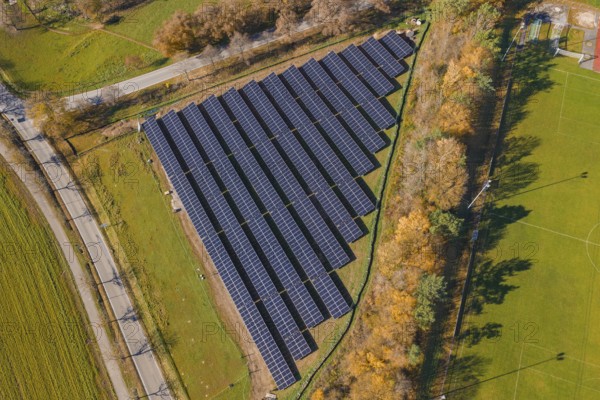 Aerial view of a solar plant surrounded by green fields and autumn trees, PV Freifaechenanlage