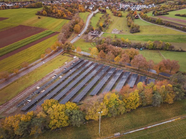 Large-scale solar plant near a village, surrounded by autumnal fields, Bau PV Freifaechenanlage,