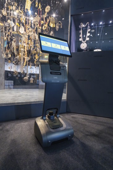 A robot with a screen stands in front of a glass display case with decorative objects in a museum,