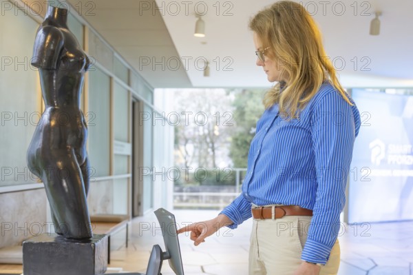 Woman operating a device in front of a statue in a modern exhibition room, robotic personality