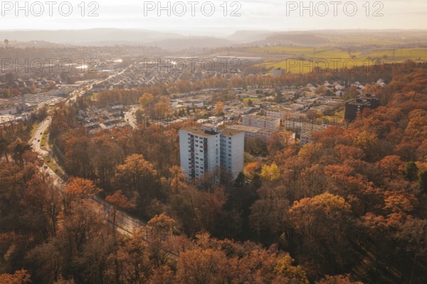 A residential building towers over an autumnal forest with a town behind it, MÃ¼hlacker, Enzkreis,